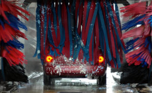 A view from inside of the car wash of a red sedan being washed.